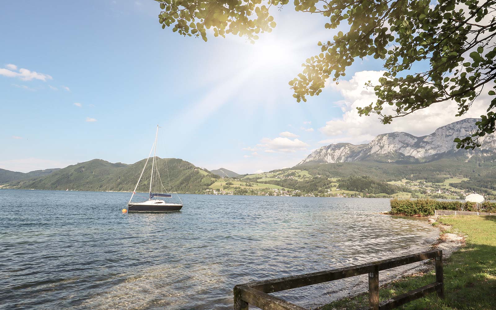 Ein Segelboot ankert in Ufernähe am Attersee in Oberösterreich. Die Sonne strahlt.